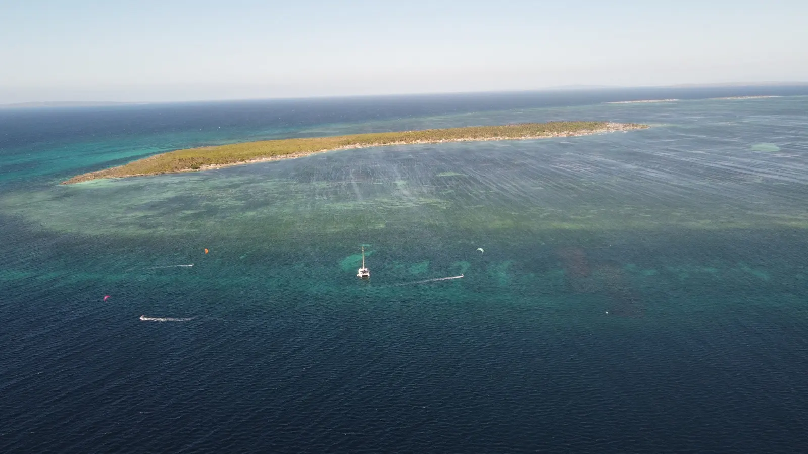 Similar anchorage scene, kitesurfers and jetskis near reef island
