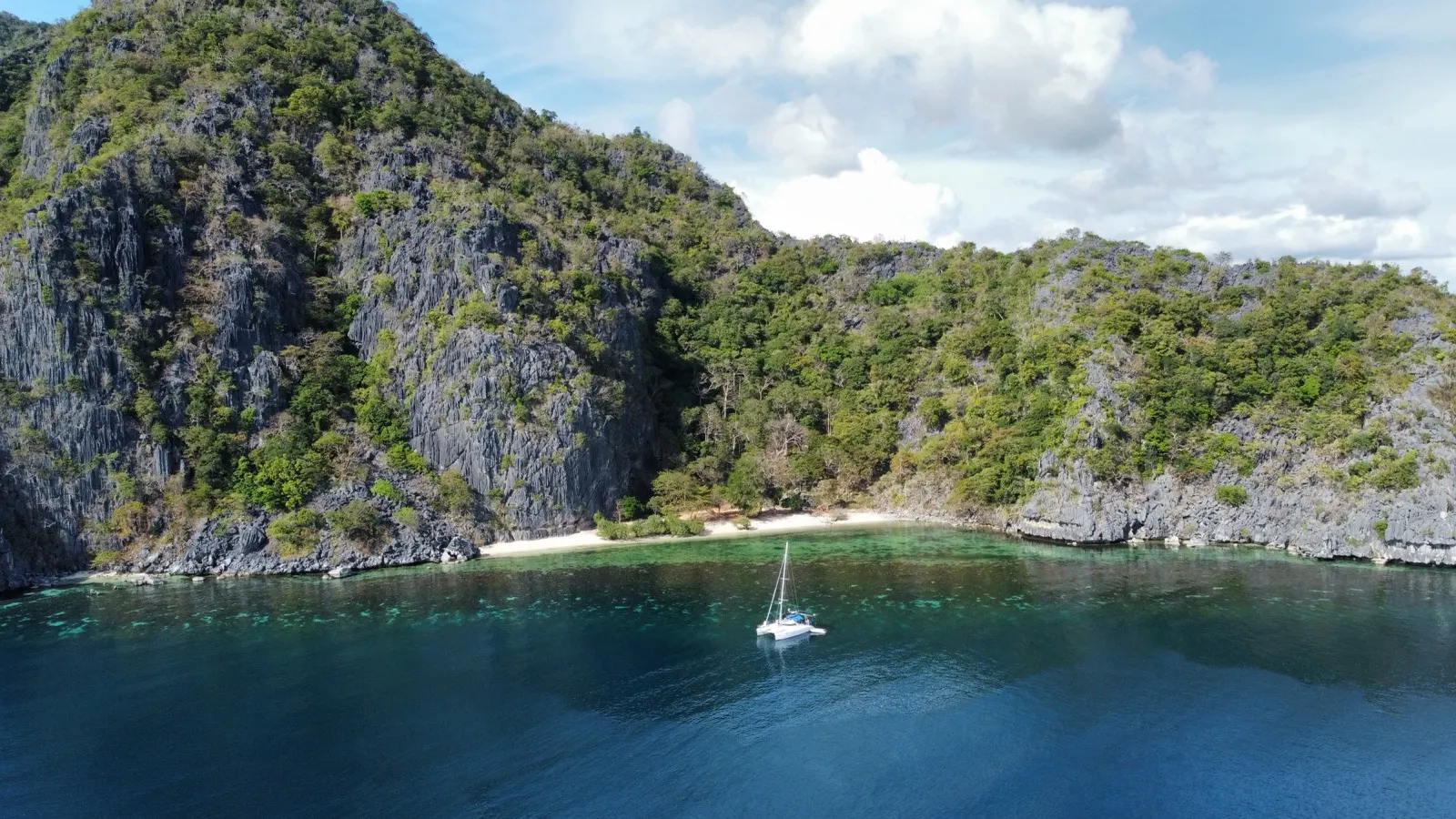 Catamaran anchored in cove beneath limestone cliffs
