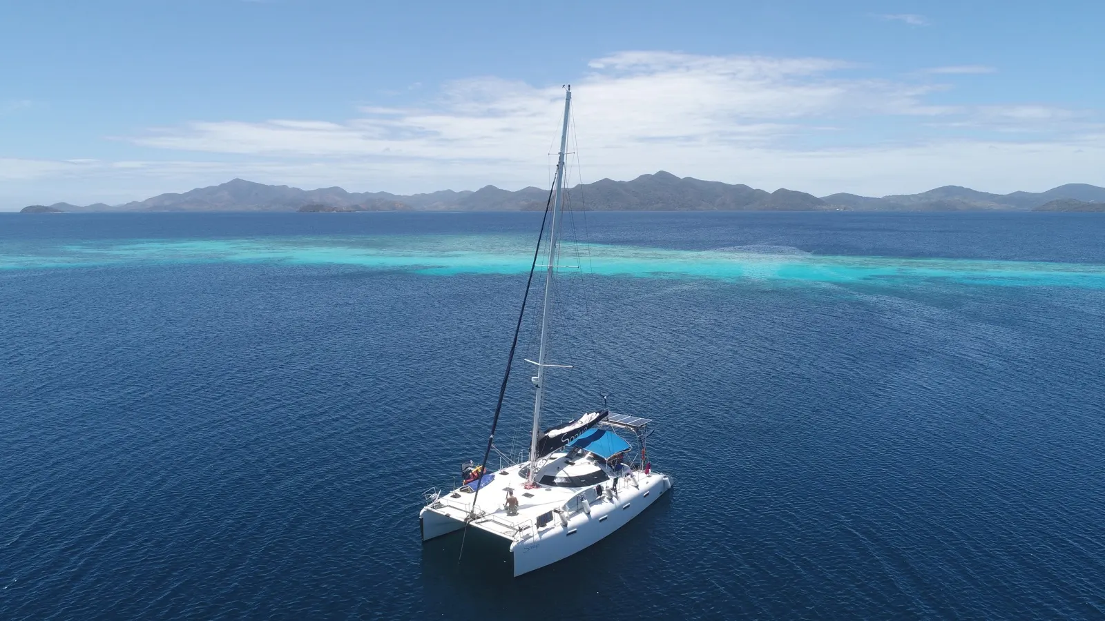 Soniya under sail with mainsail up, mountains and reef backdrop