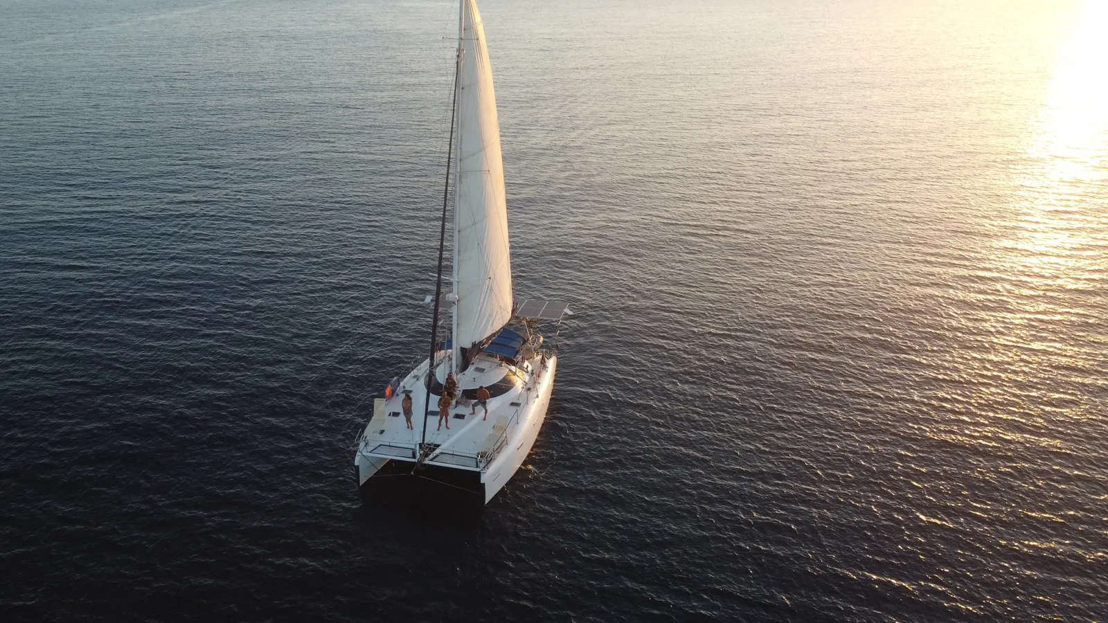 Solo aerial of Soniya sailing at dusk, backlit water