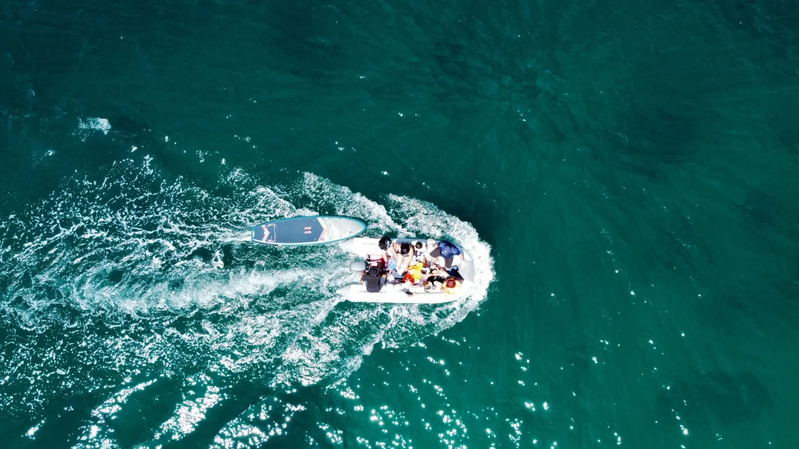 Aerial top-down of dinghy speeding across turquoise water