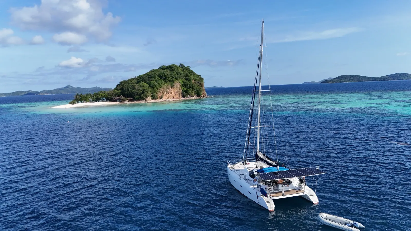 Wide aerial, island beach, catamaran with local boats