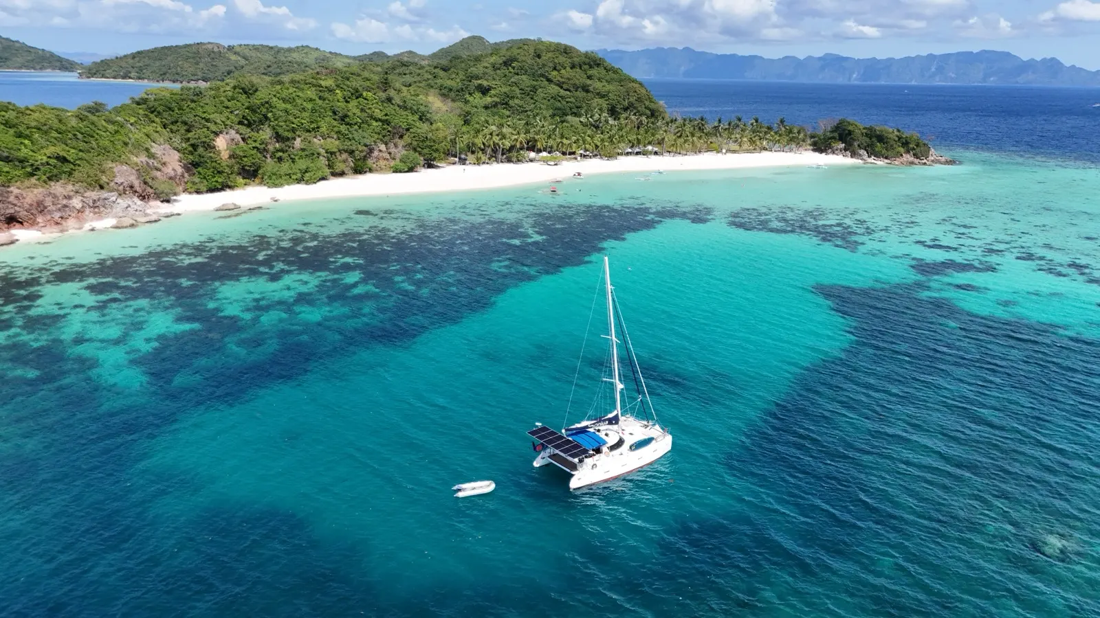 Wide aerial, island, catamaran anchored near reef