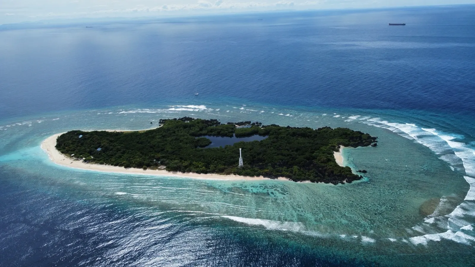 Small atoll island with lighthouse, reef ring, distant ships