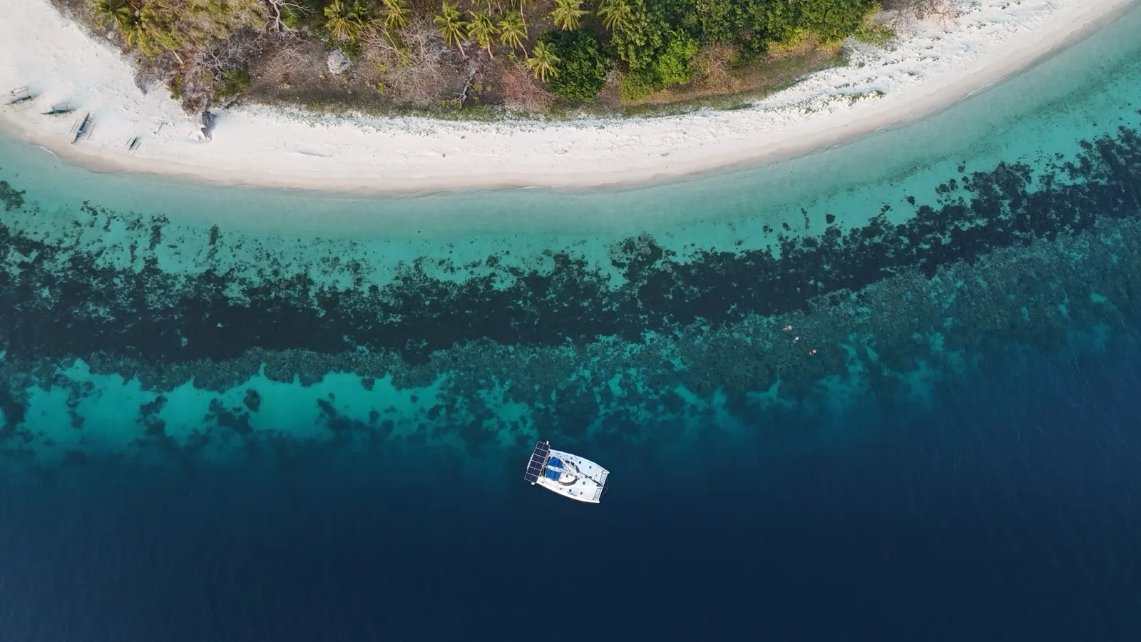 Aerial of island sandbar, reef, and anchored catamaran