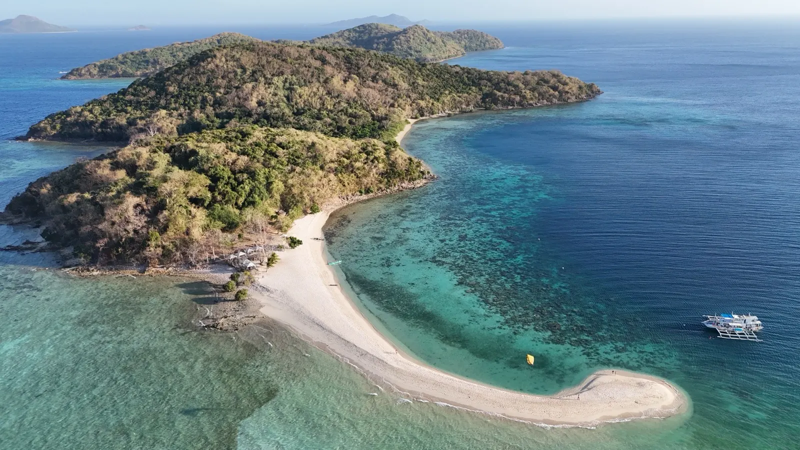 Aerial of curving sandbar island with reef and boat