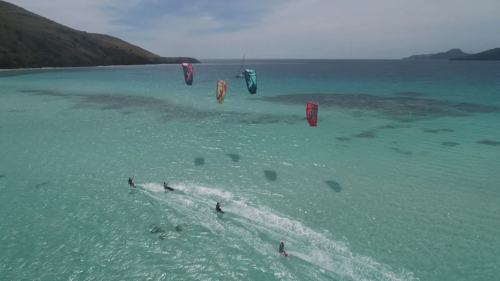 Four kitesurfers riding together in turquoise water