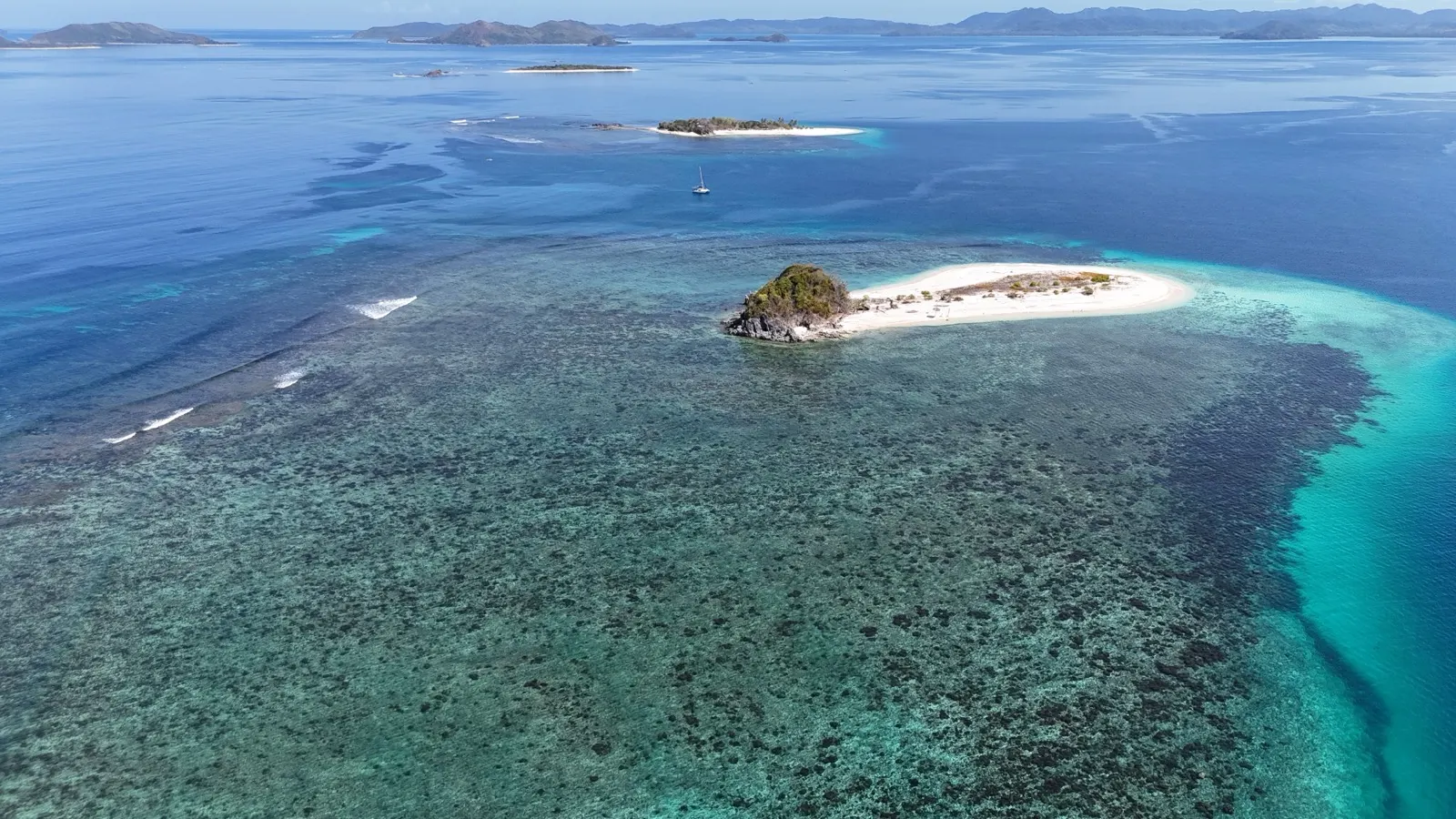 Aerial of scattered islands and reef, distant sailboat