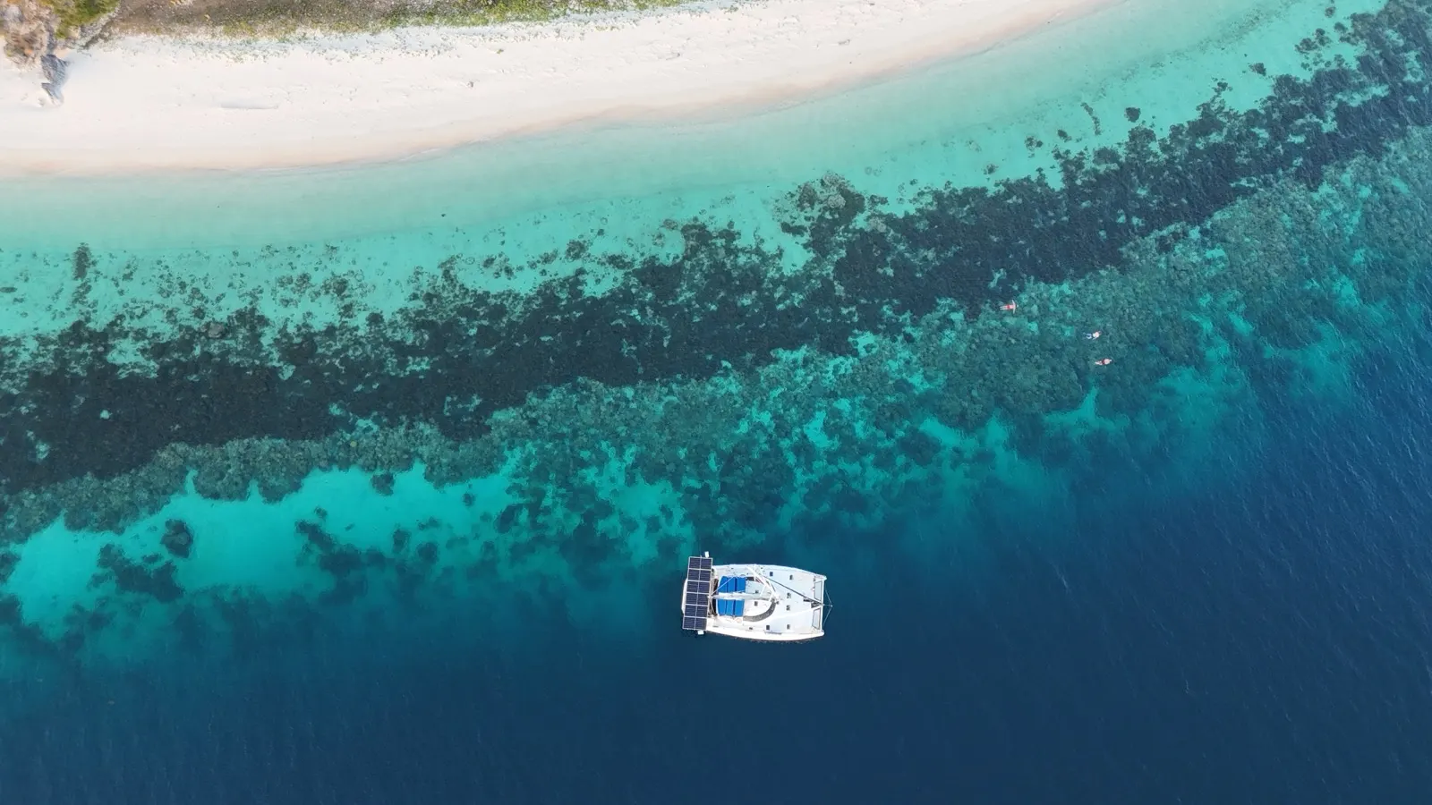 Aerial of catamaran anchored beside reef and sandbar