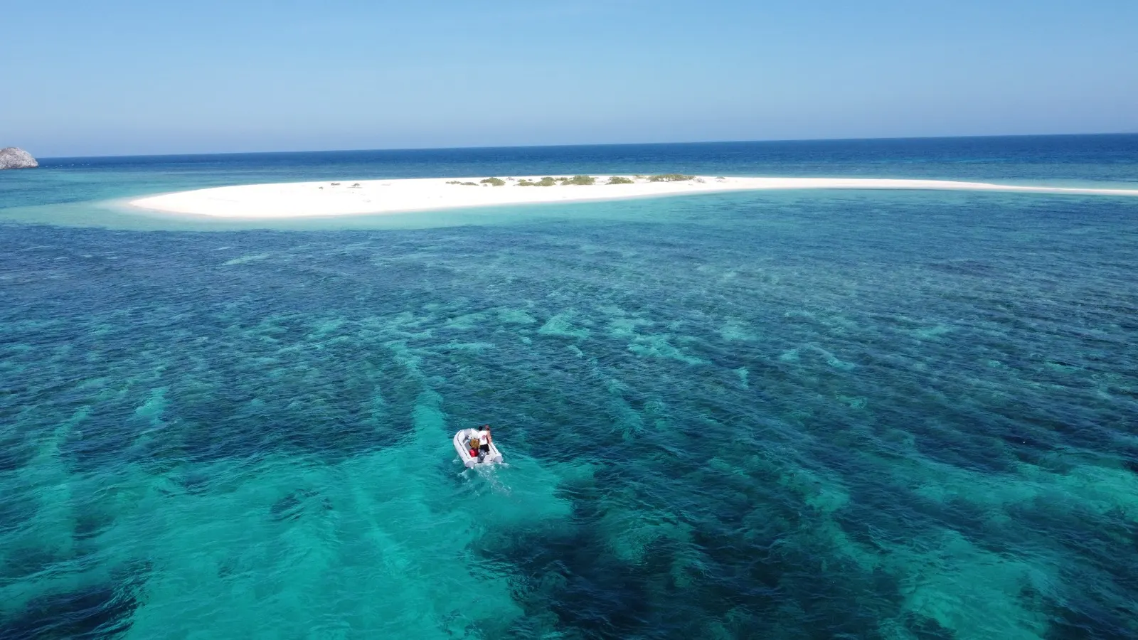 Dinghy with two people arriving at a white sandbar