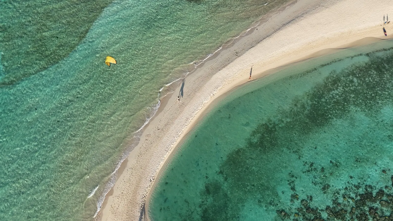 Aerial of sandy spit, reef, kite and beachgoers