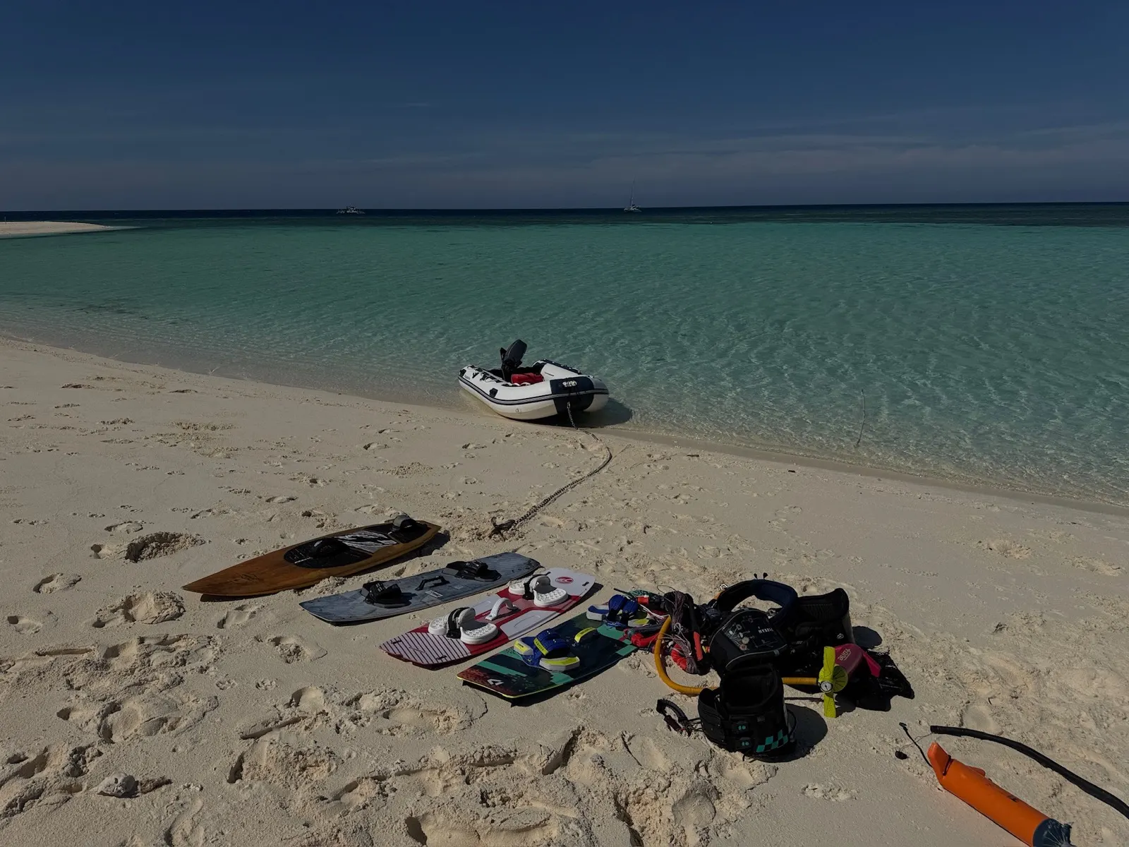 Kite gear and boards laid out on sandbar with dinghy and yacht