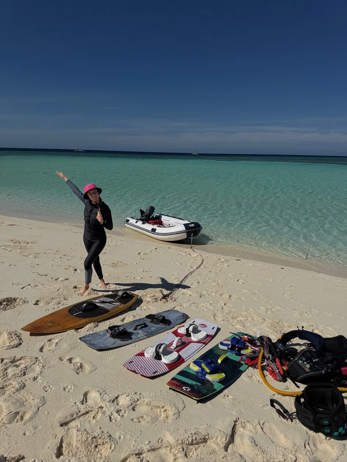 Woman posing beside kite gear on sandbar, dinghy behind