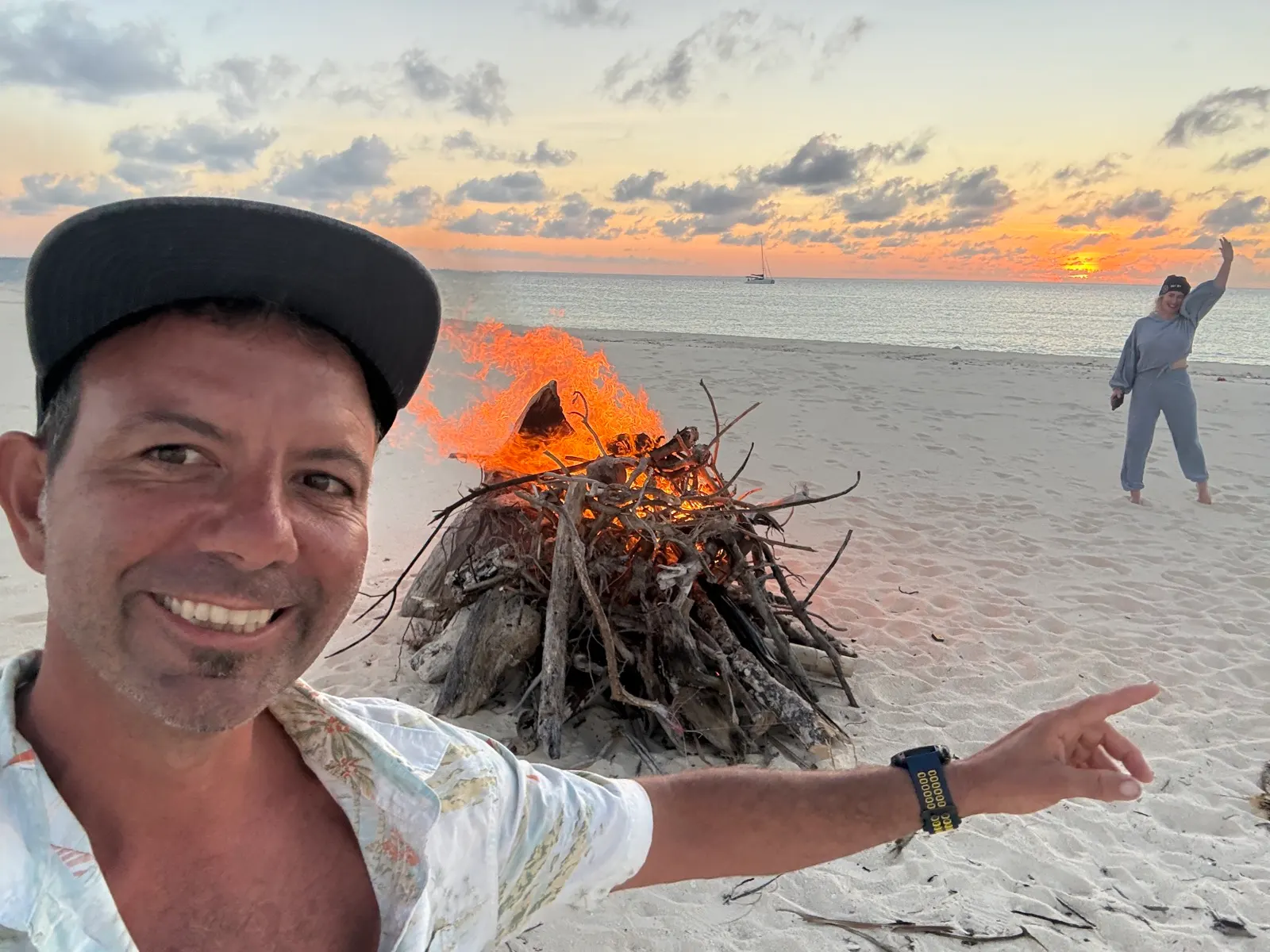 Man mid-flip on beach near driftwood bonfire at dusk