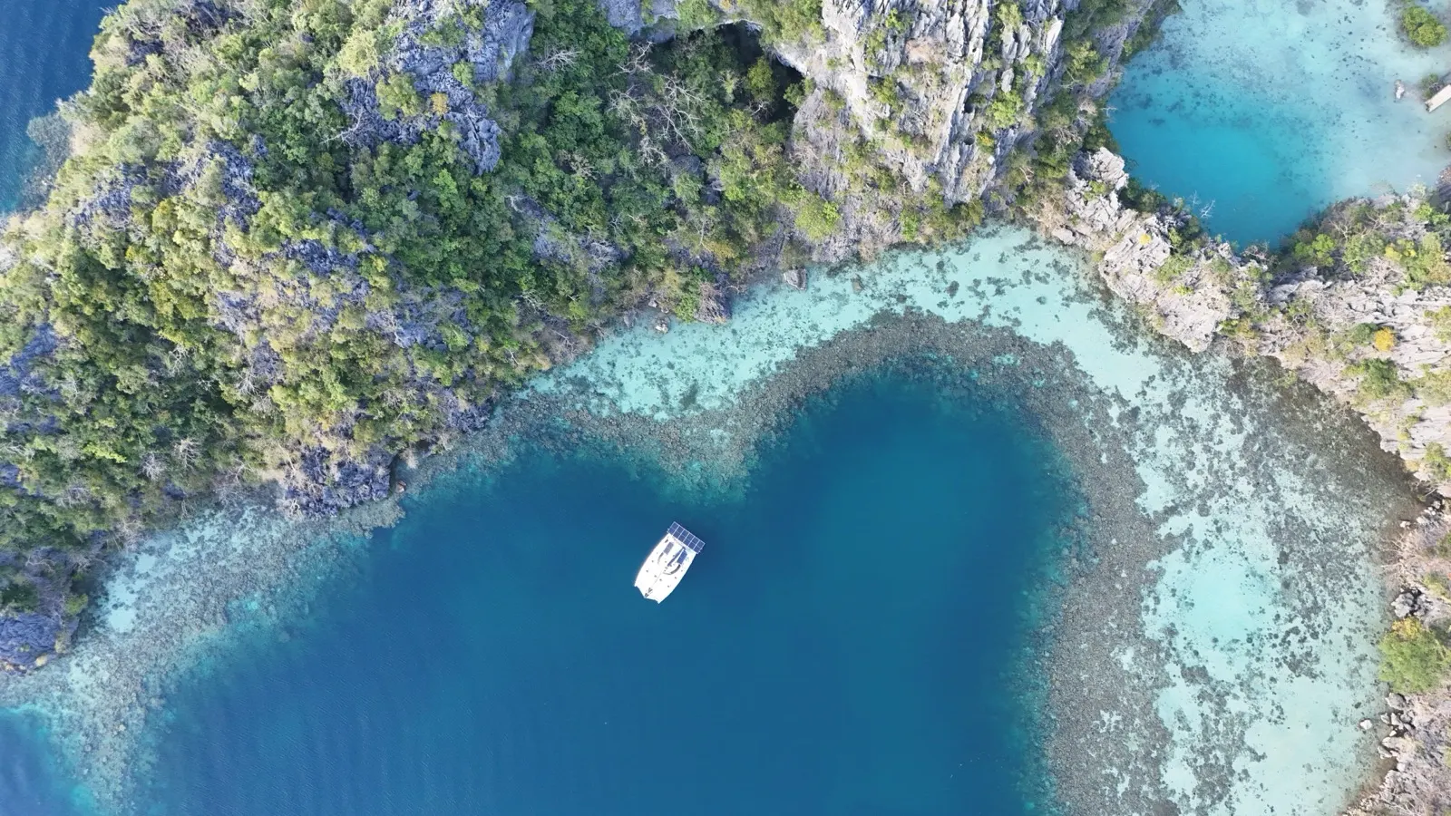 Top-down catamaran anchored in blue limestone lagoon