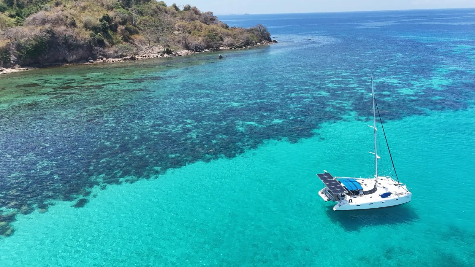 Catamaran near reef edge, island cliffs in background