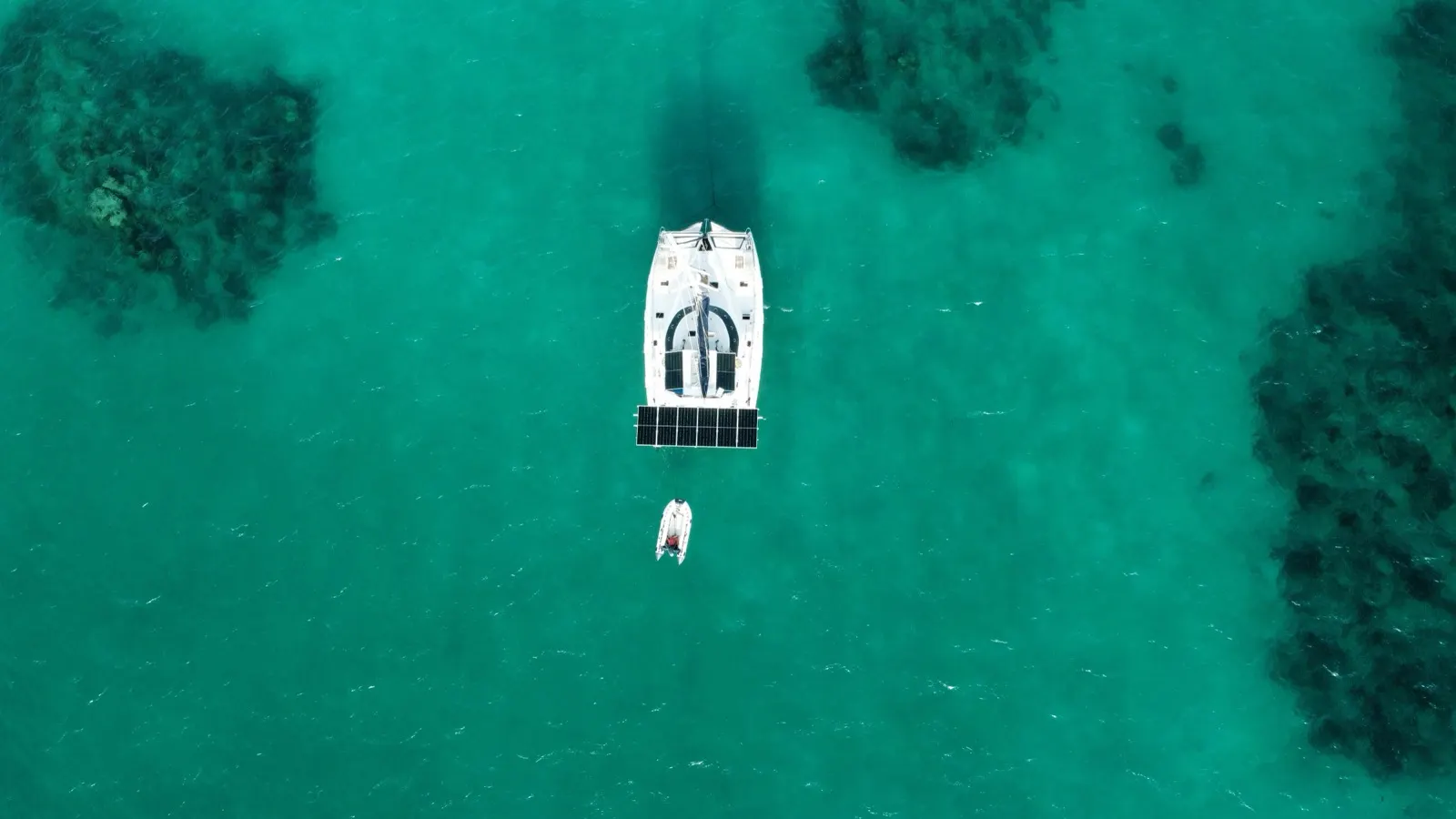 Top-down catamaran and dinghy anchored by reef