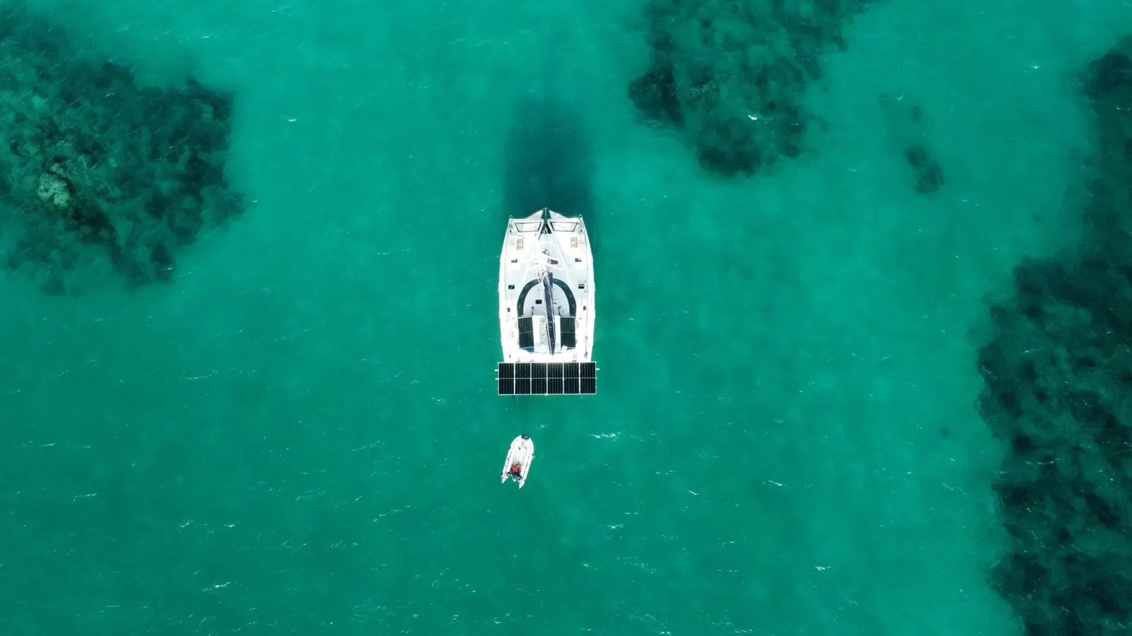 Near-duplicate top-down catamaran and dinghy over reef