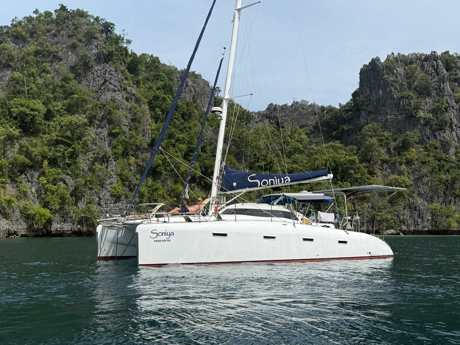 Soniya anchored beside limestone cliffs, person lounging