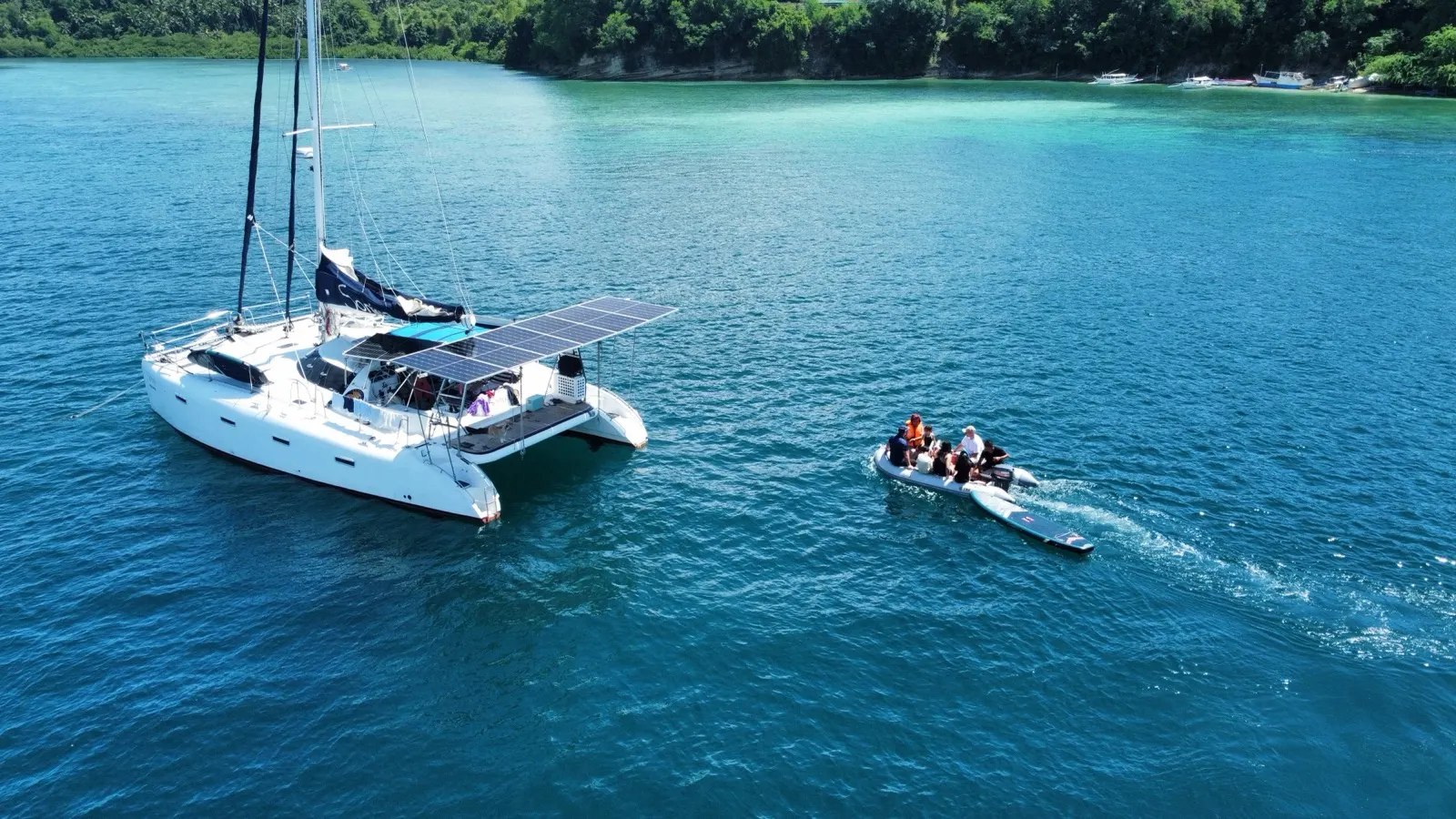 Catamaran with people aboard, dinghy alongside