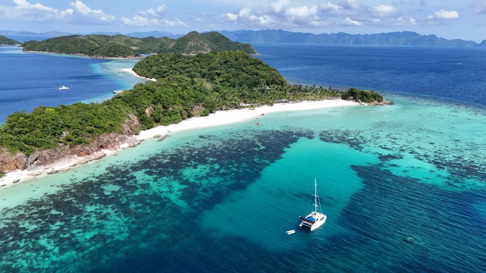 Catamaran close to small green island, sails up