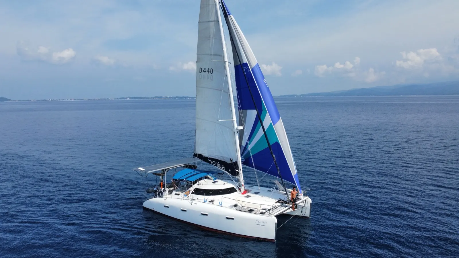 Soniya under sail with spinnaker, crew member at stern