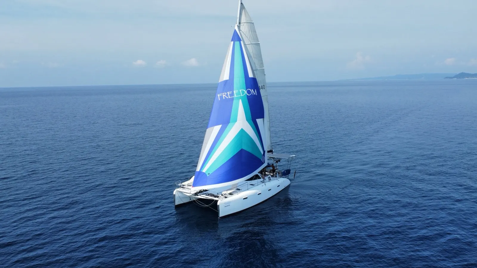Aerial of catamaran under spinnaker, sunlit water