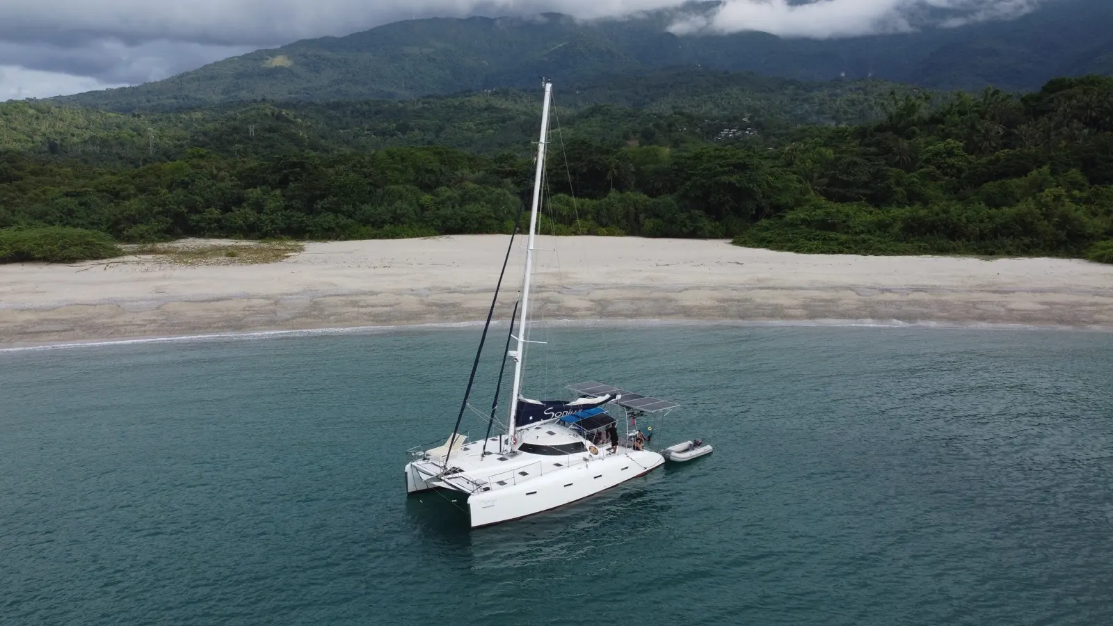 Catamaran anchored off jungle beach, moody stormy sky