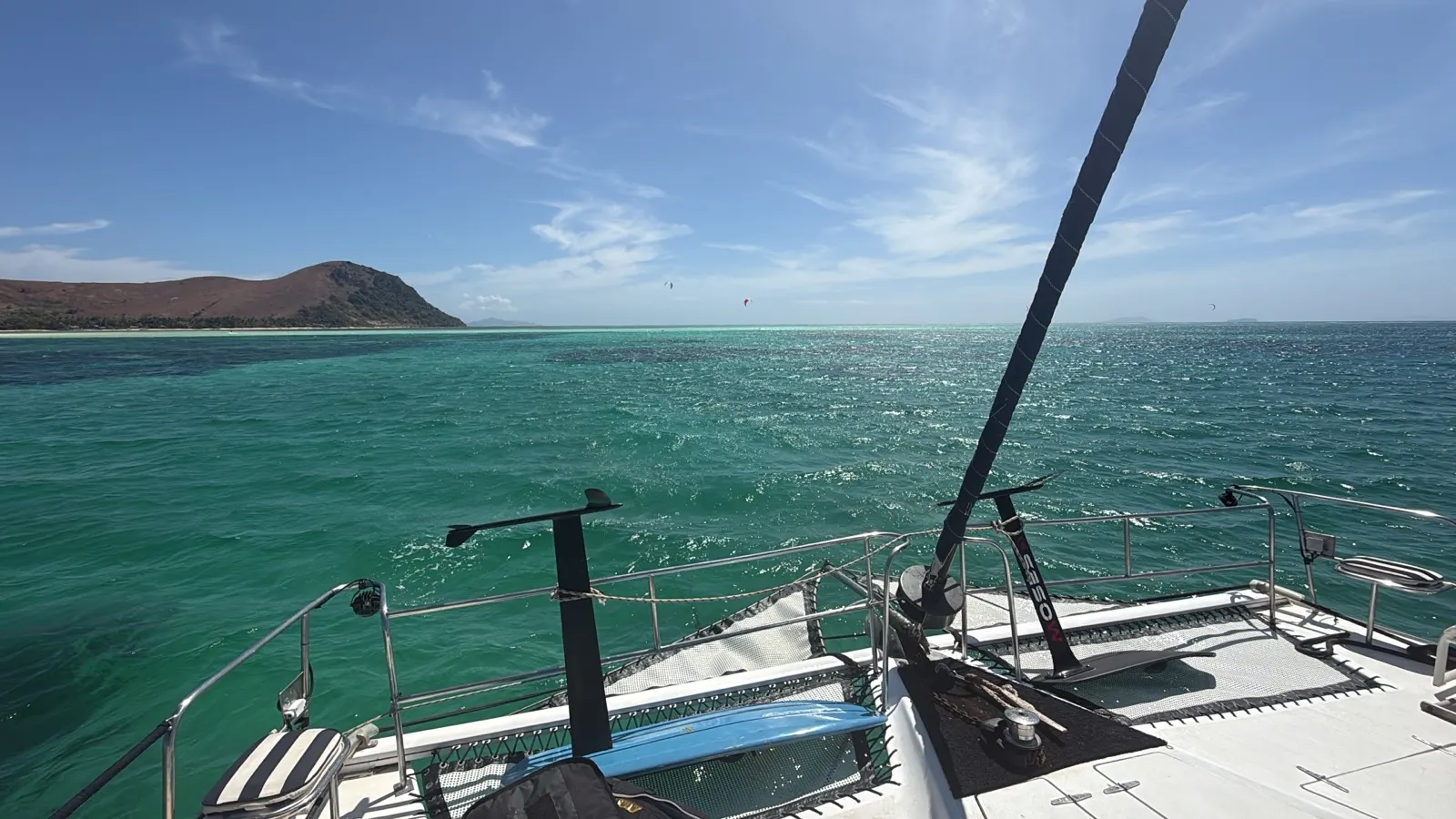 View from catamaran bow with distant kites and coastal hills