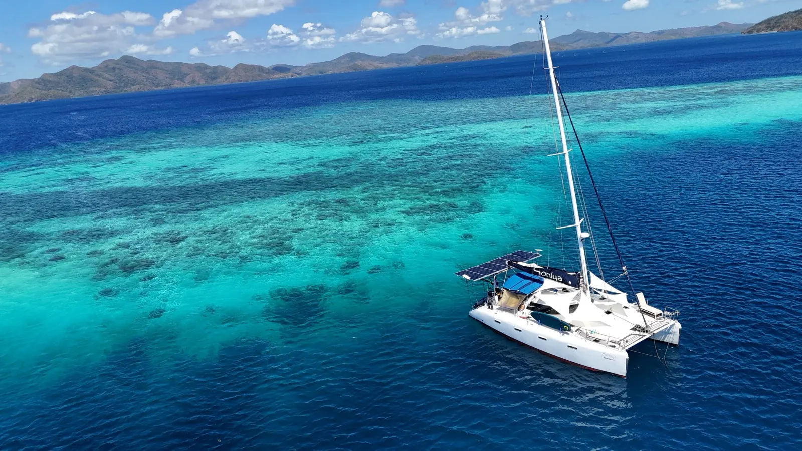 Dinghy crossing shallow reef toward jungle shoreline