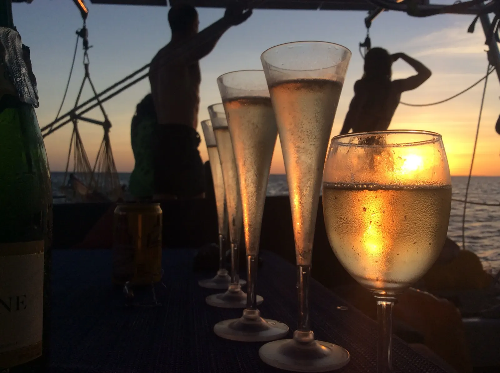 Champagne flutes glowing at sunset, crew silhouetted
