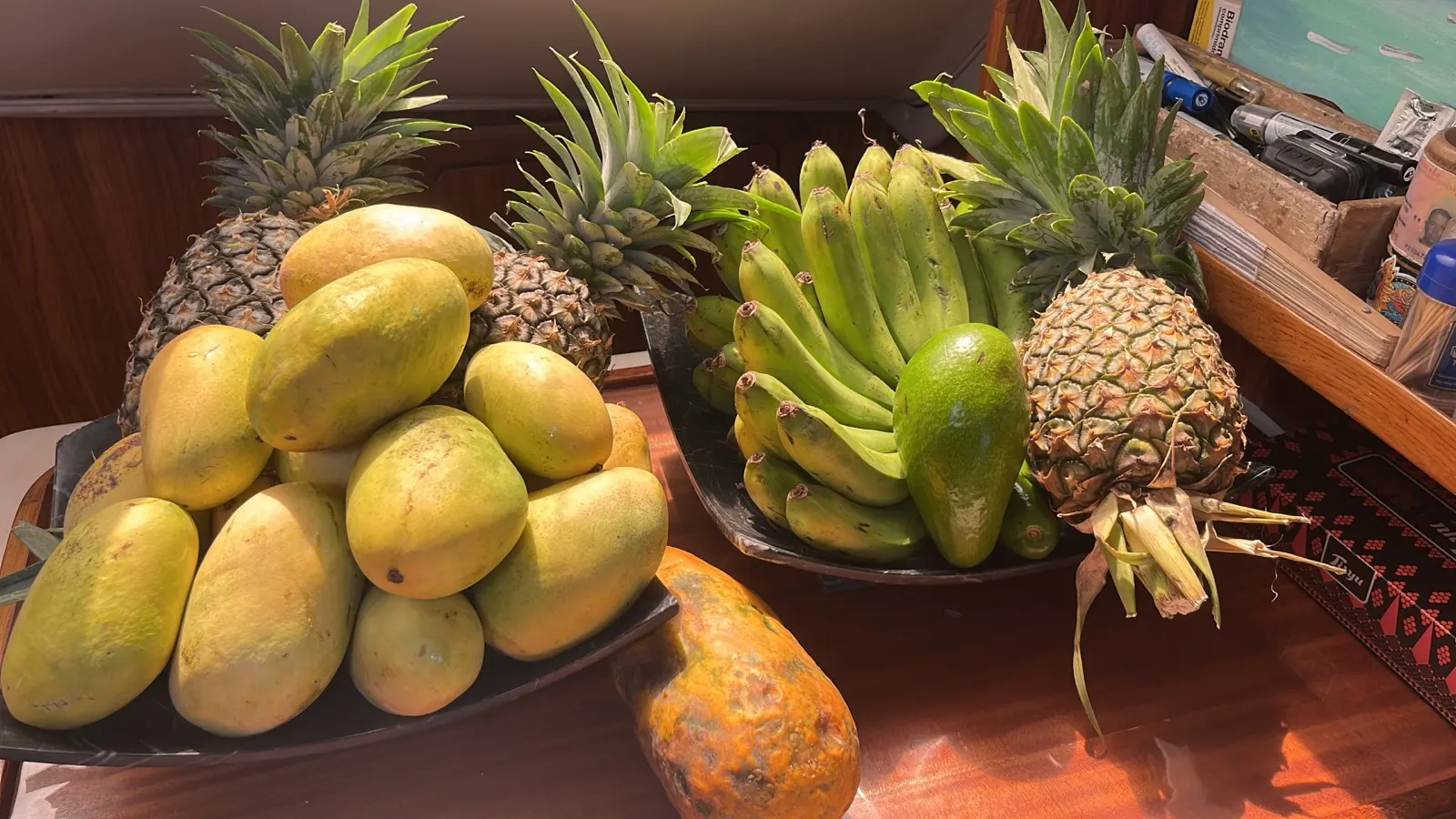 Fresh mangoes, pineapples, bananas, avocado on a table below deck