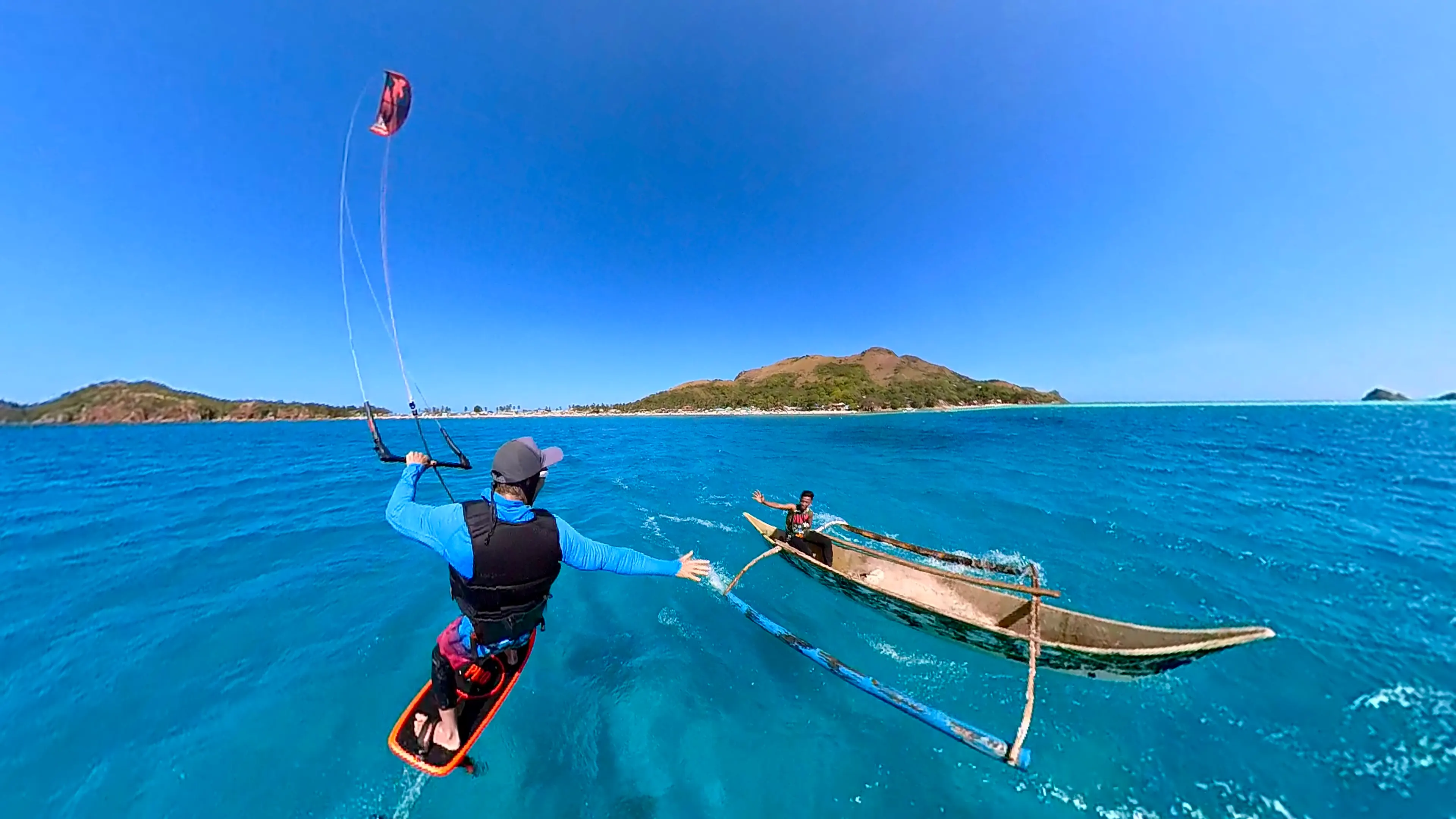 Kiteboarder jumping alongside a traditional outrigger banca, fisherman waving