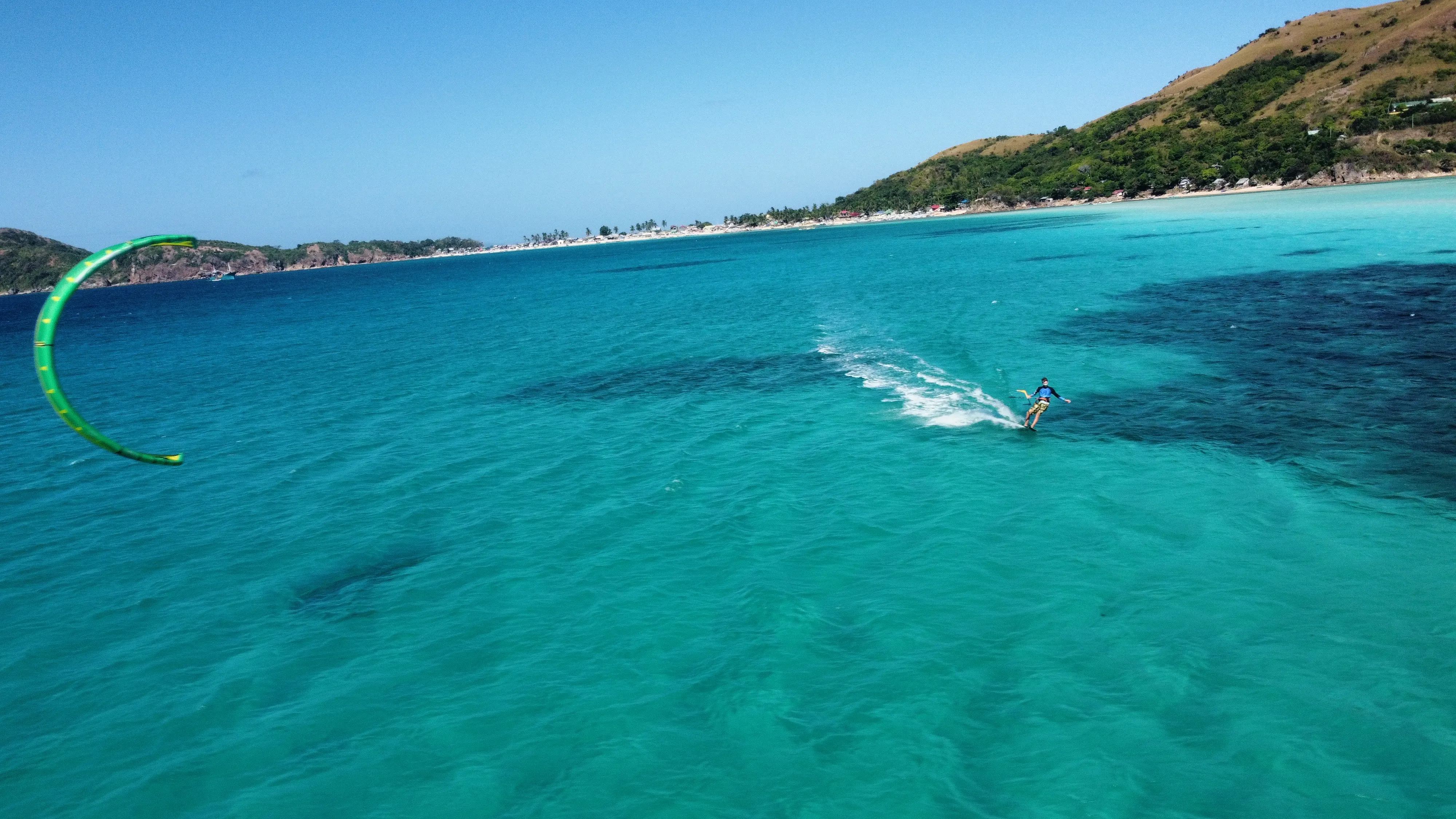 Kiteboarder riding a turquoise bay with green kite