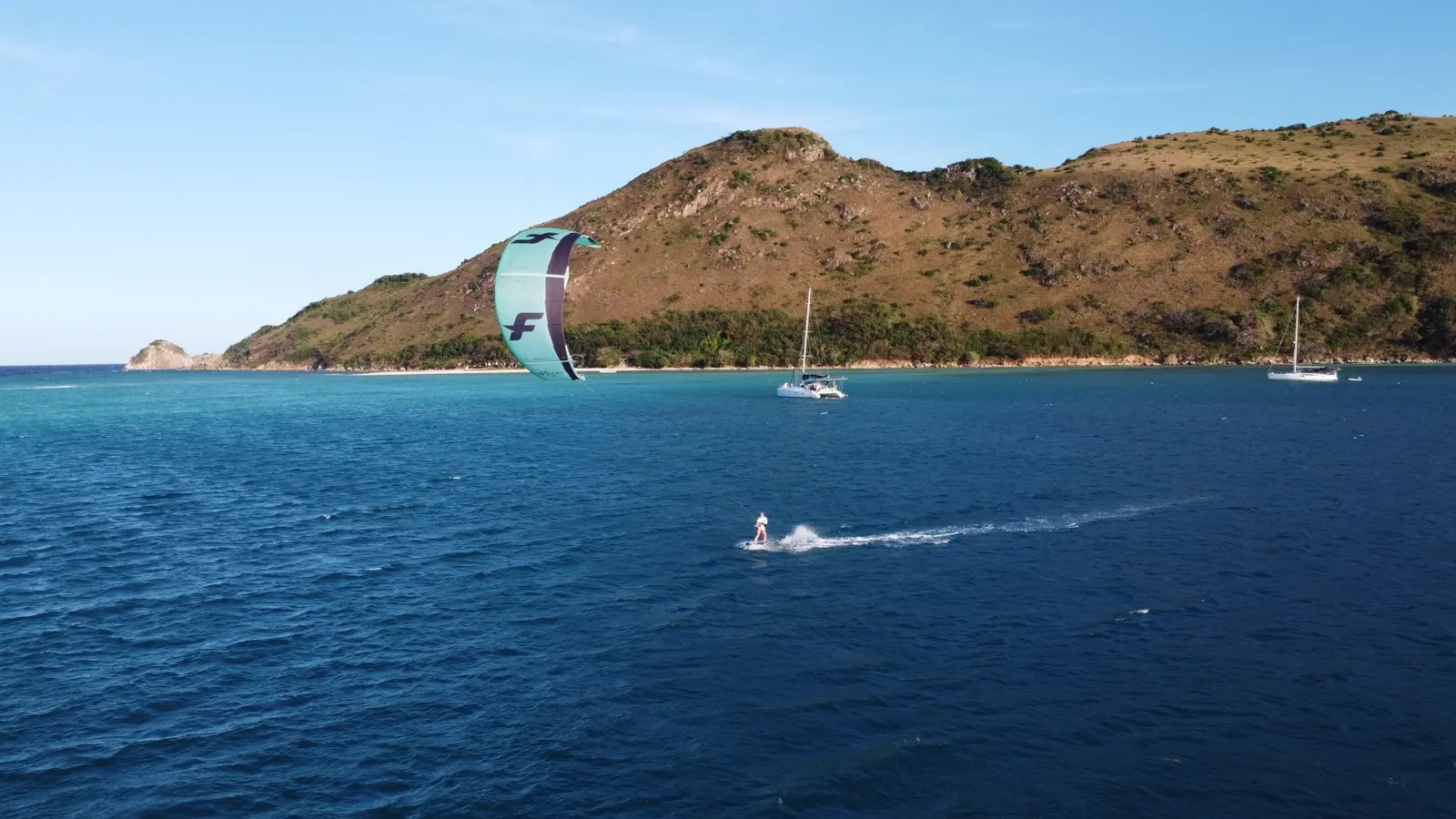 Kitesurfer riding, catamaran and sailboat distant