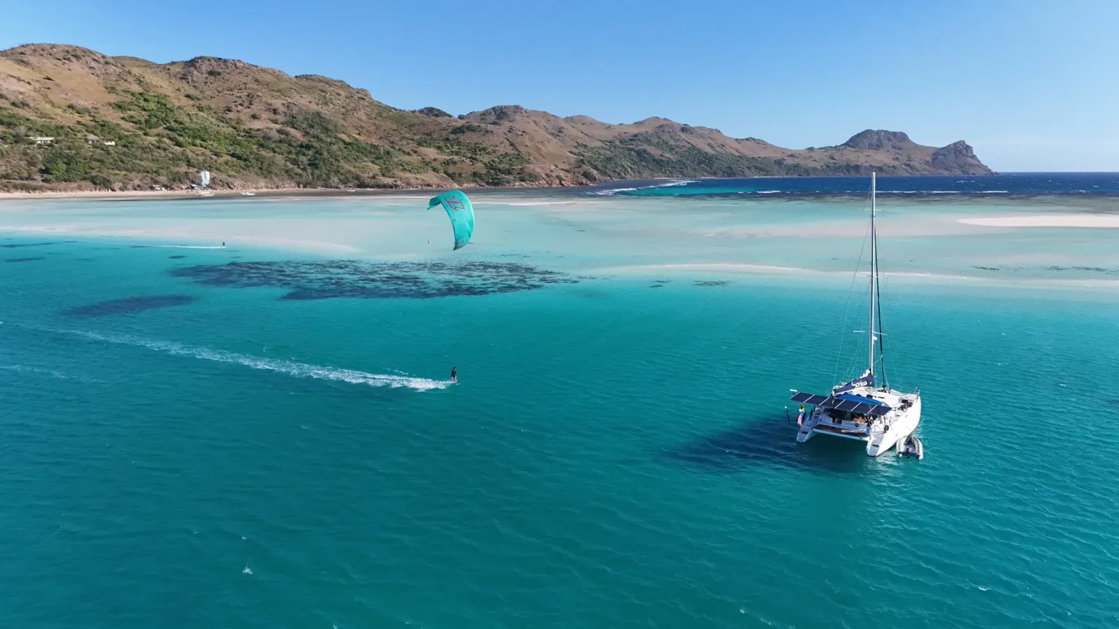 Catamaran anchored, kitesurfer riding past