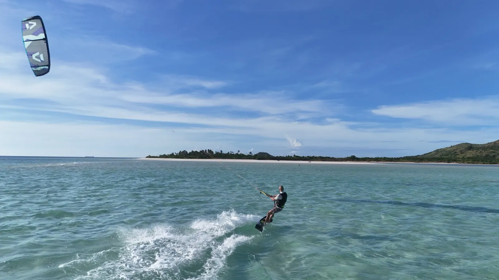 Kitesurfer riding toward a white sand beach