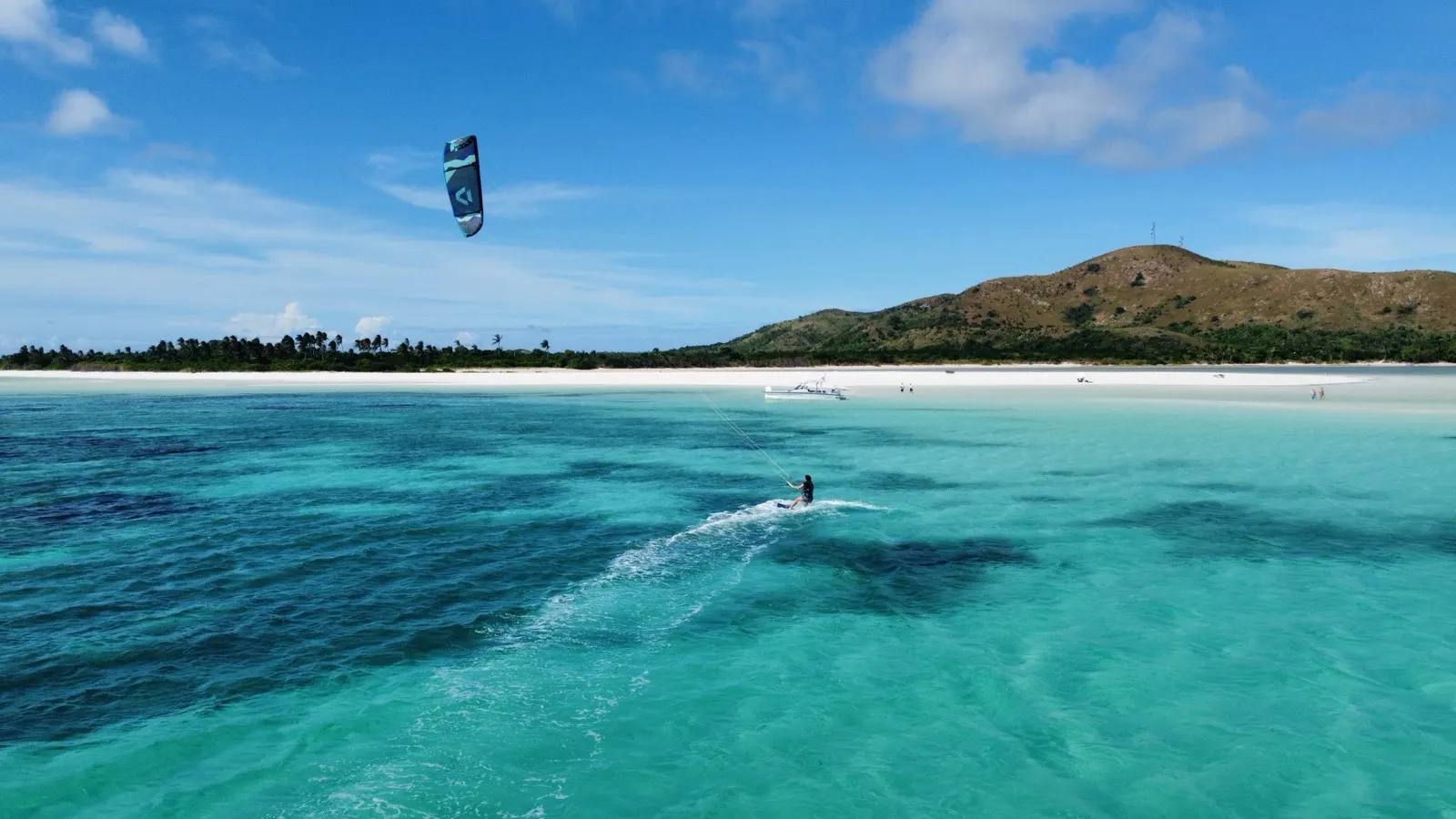 Kitesurfer riding turquoise water near a white sandbar beach