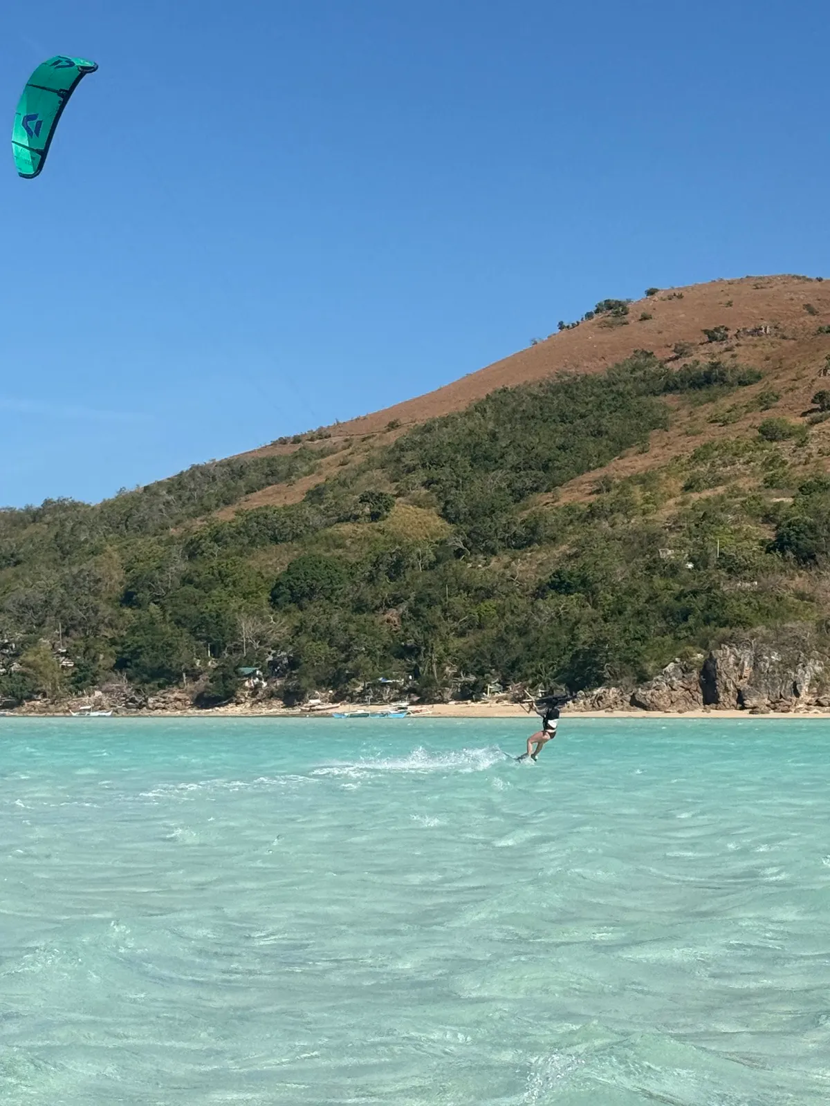 Aerial shot of kiter walking beach, coastal village behind