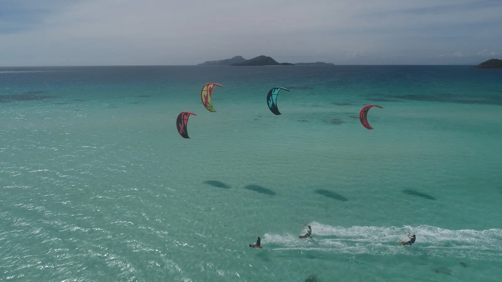 Four kitesurfers riding turquoise water, island on horizon