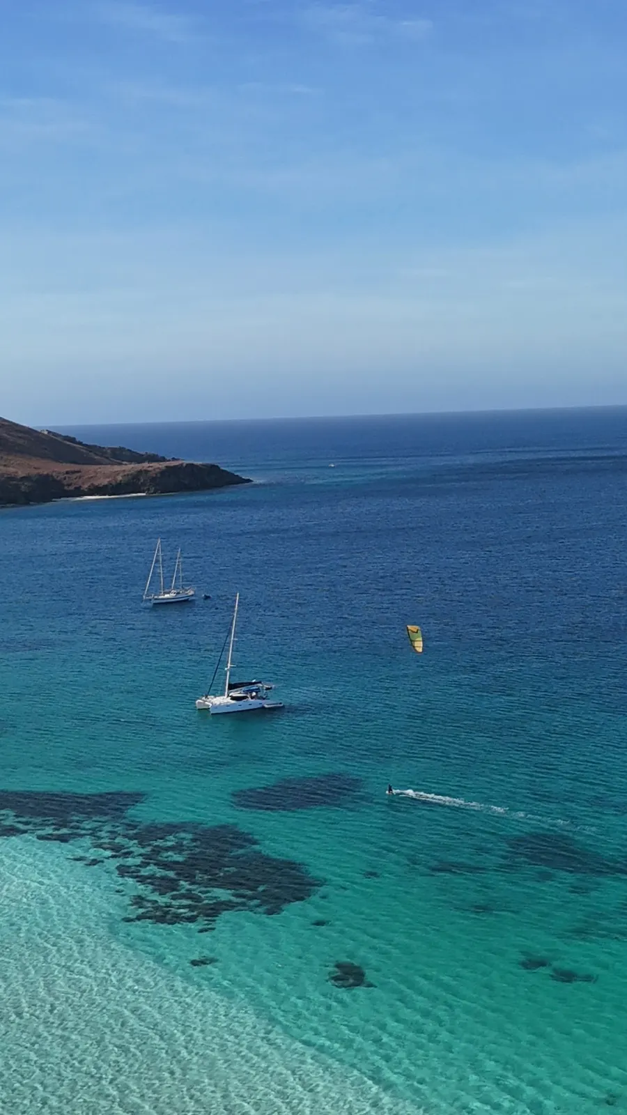 Kitesurfer near catamaran with mountainous island backdrop