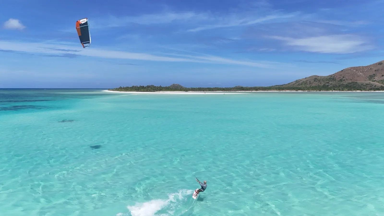 Kitesurfer riding across turquoise lagoon toward beach