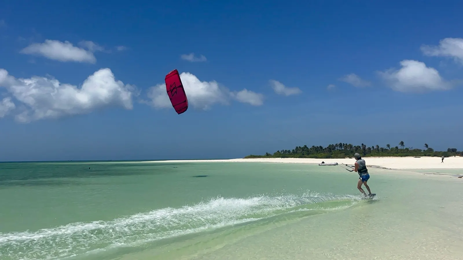 Kitesurfer approaching sandbar with dinghy and people