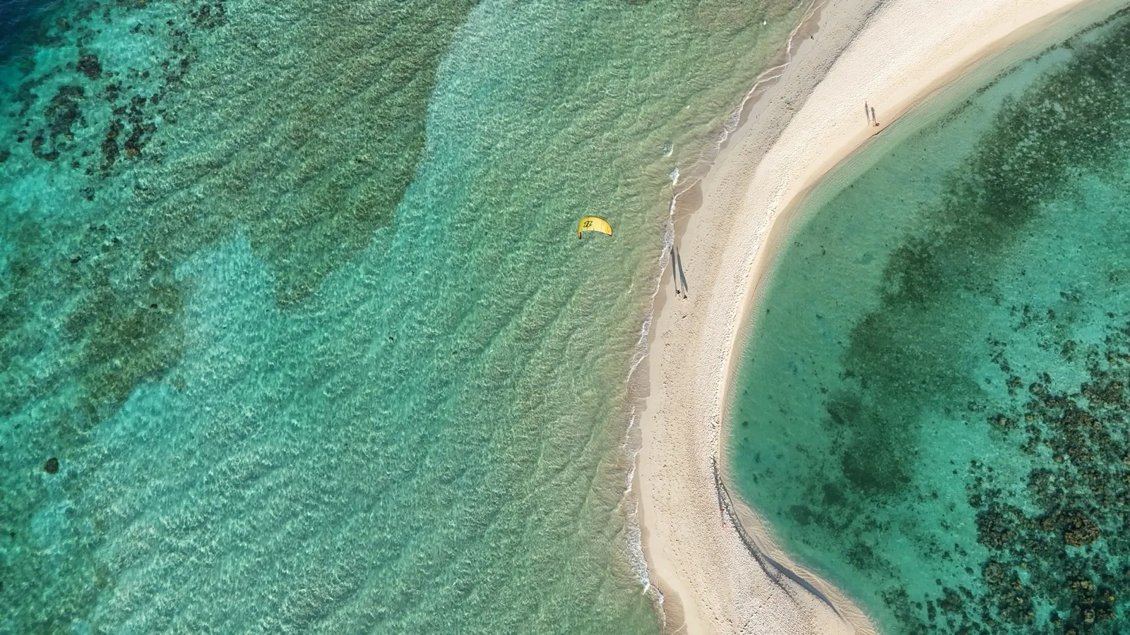 Yellow kite over sandbar with people walking