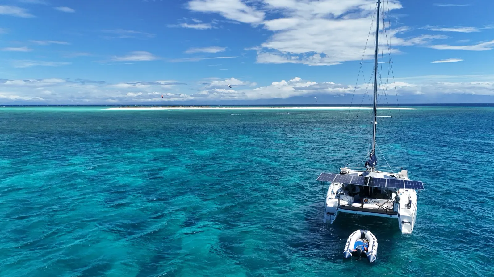 Catamaran anchored off reef island, kitesurfers in distance
