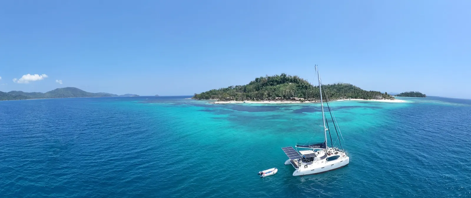 Panorama of catamaran near jungle-covered island