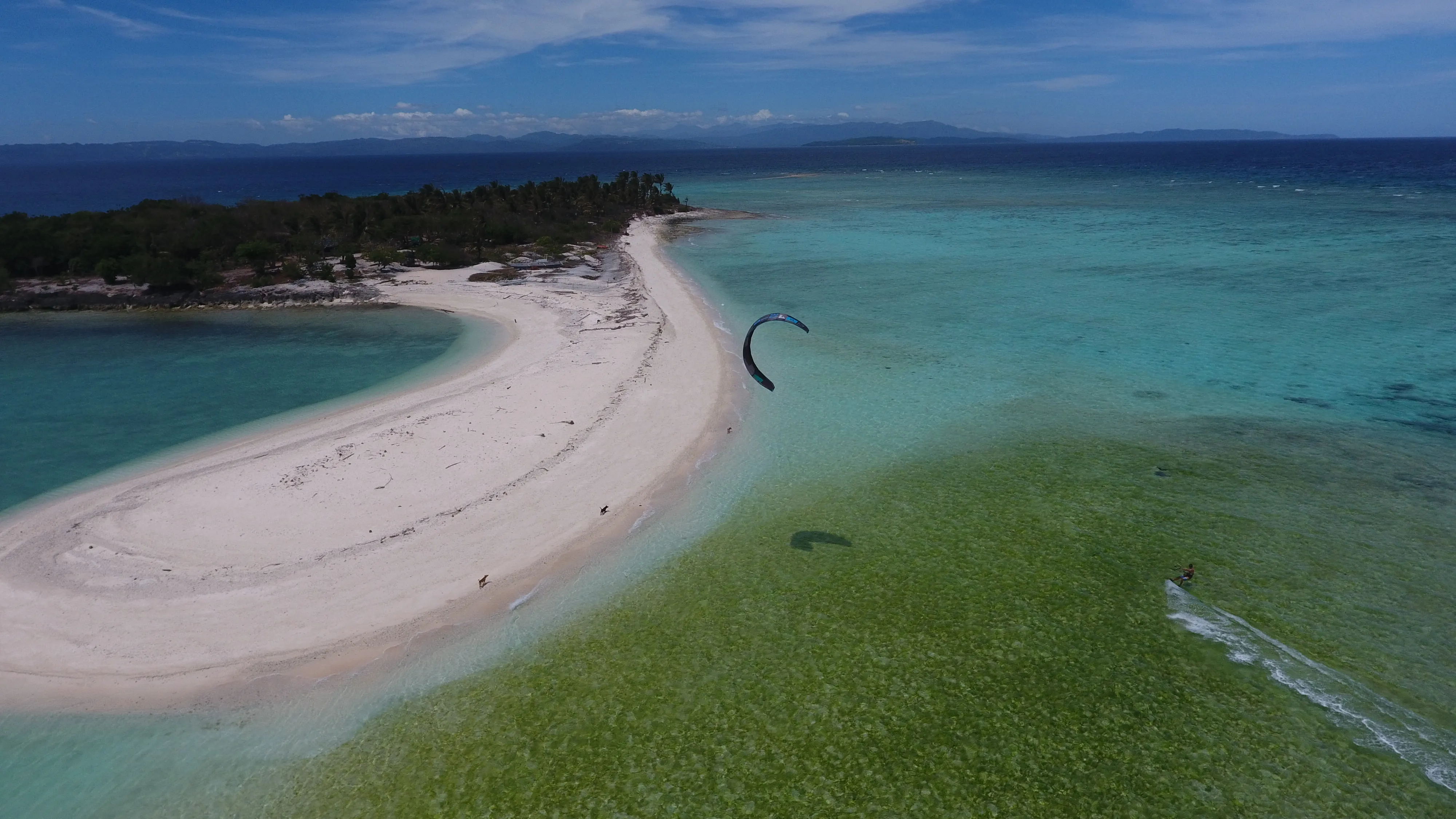 Kitesurfer riding through a lagoon beside a curved Mindoro sandbar