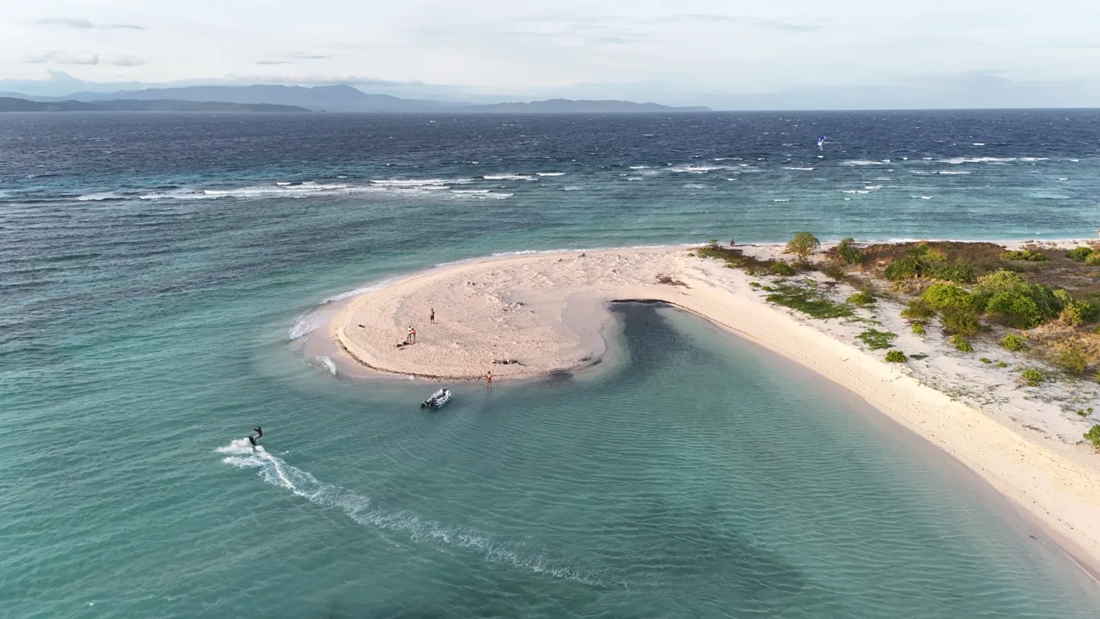 Aerial of sandbar with kitesurfer, people, and dinghy