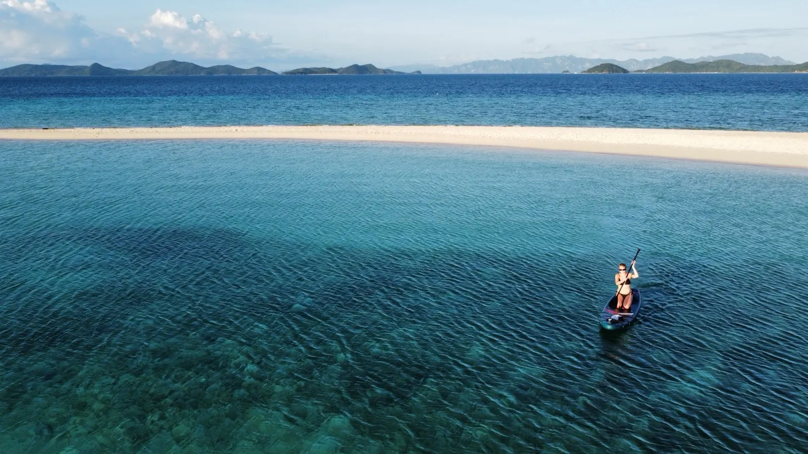 Woman paddleboarding near sandbar, dusk light