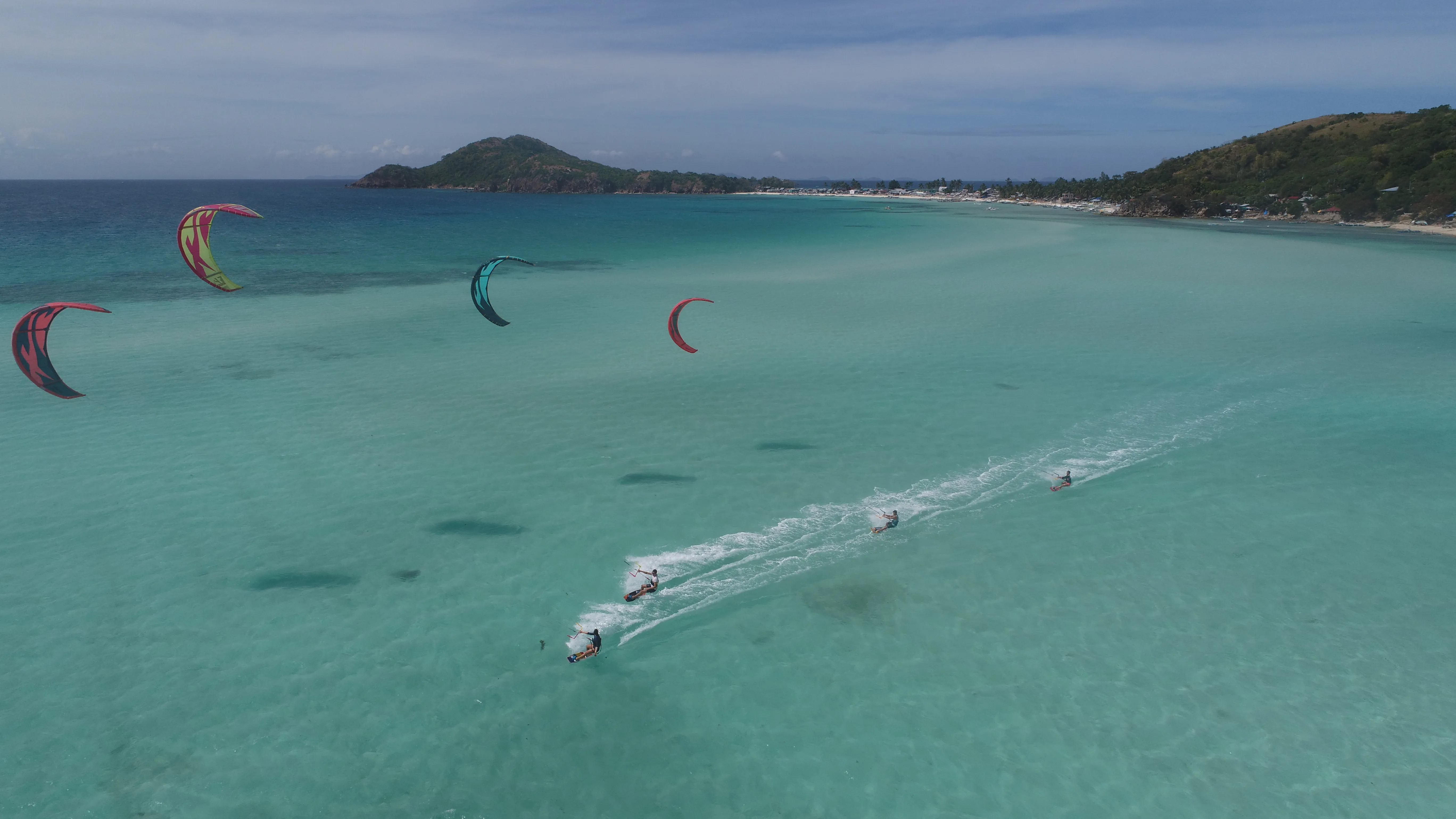 Aerial view of multiple kitesurfers riding together over a Palawan reef